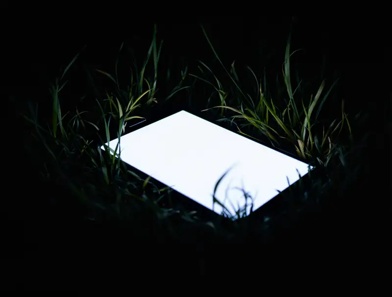 A phone lying face up in the grass at night, its screen glowing.